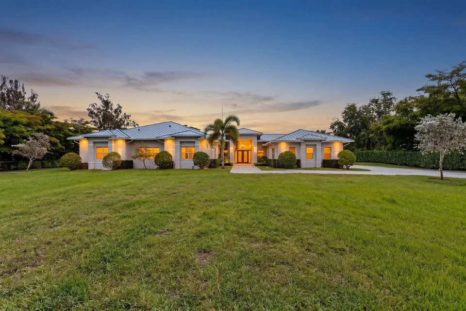 Single-story home with a broad lawn and warm exterior lighting at dusk
