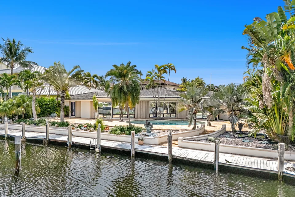 Waterfront home with palm trees, a dock and a boat beside the canal